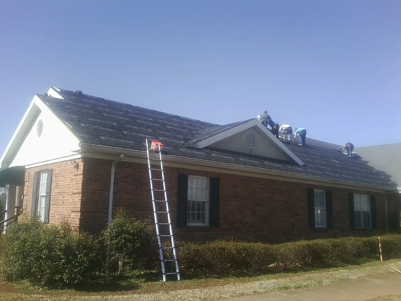 Crew tearing shingles off a brick ranch roof with a ladder set — Metal Roof Repair work by our crew in Bridgeton
