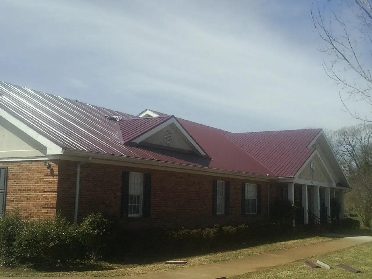 Red metal roof with gabled entries on a long brick building, from a Hail Damage Roof Repair job in Bridgeton