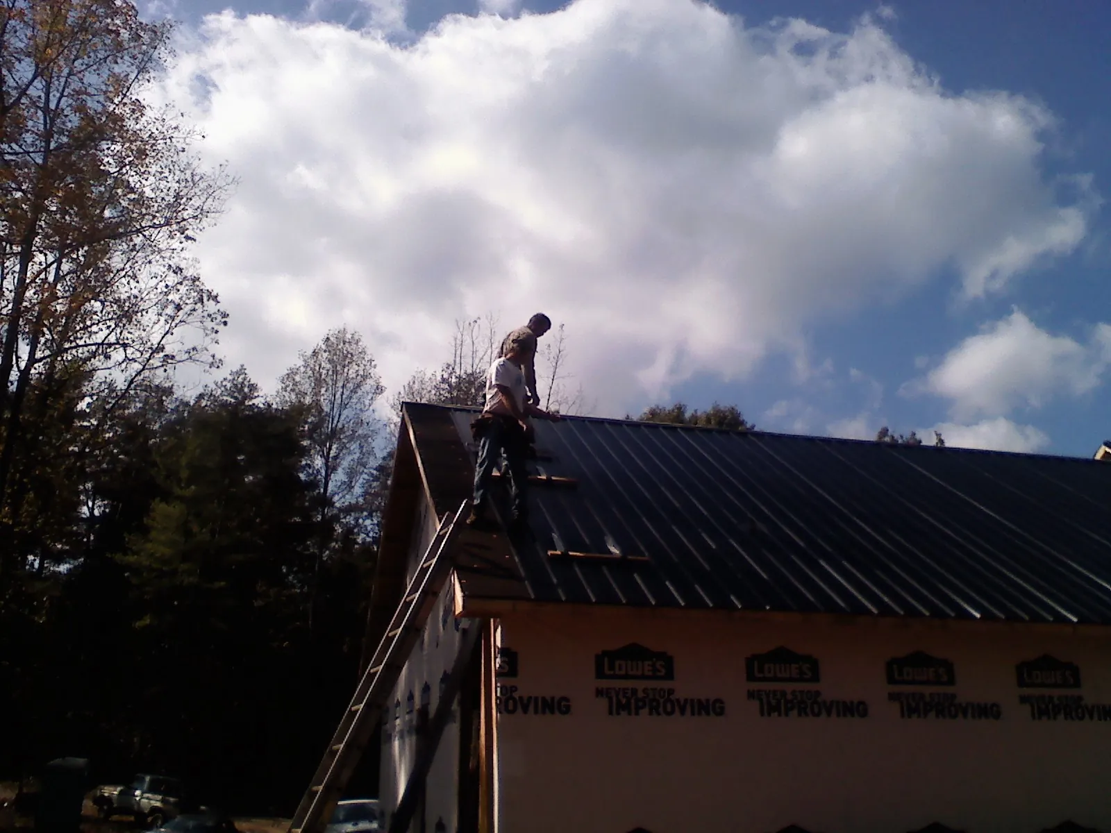 Roofer fastening dark metal panels high against a cloudy sky, from a Roof Inspection job in Bridgeton